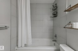 Bathtub with tiled surround, chrome fixtures, and wall-mounted shelving - 