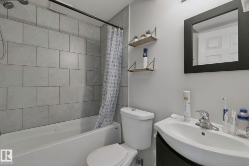 White porcelain tub with light gray tile surround, wall-mounted showerhead, and black shower rod - 8535 Ellis Link Link Nw, Edmonton, AB 