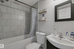 White porcelain tub with light gray tile surround, wall-mounted showerhead, and black shower rod - 