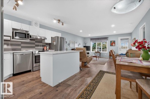 Open concept living space featuring wood-finish flooring, white cabinetry, stainless steel appliances, a white kitchen island, and recessed lighting - #125 4610 50 Ave, Stony Plain, AB 