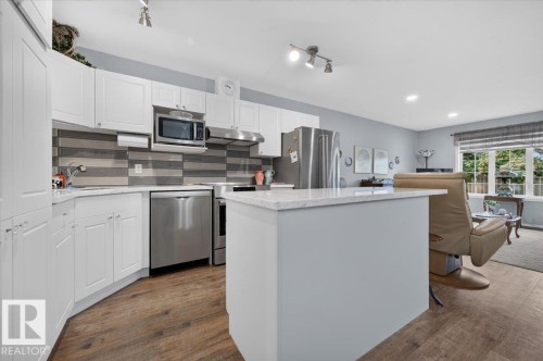 Kitchen featuring white cabinetry, stainless steel appliances, a multi-tone tile backsplash, and light-colored countertops - #125 4610 50 Ave, Stony Plain, AB 