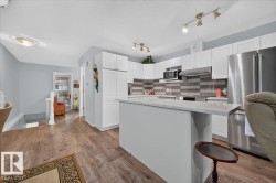 Kitchen featuring white cabinetry, a built-in microwave, stainless steel appliances, a center island with a light-toned countertop, and wood-finish flooring - 