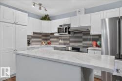 White shaker-style cabinetry, stainless steel appliances, patterned tile backsplash, track lighting, and a kitchen island with a light-colored countertop - 