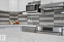 White cabinetry, stainless steel appliances, patterned tile backsplash, under-cabinet microwave, and a stainless steel range hood - 