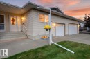Exterior featuring light-colored siding, a two-car garage with panel doors, a concrete walkway, and a landscaped lawn area - #125 4610 50 Ave, Stony Plain, AB 