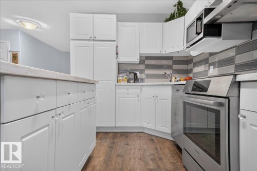 White cabinetry with crystal hardware, wood-finish flooring, full suite of stainless steel appliances, and a tiled backsplash - #125 4610 50 Ave, Stony Plain, AB 