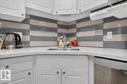 White cabinetry with crystal knobs, stainless steel undermount sink, solid surface countertops, and a multi-tone tile backsplash - 