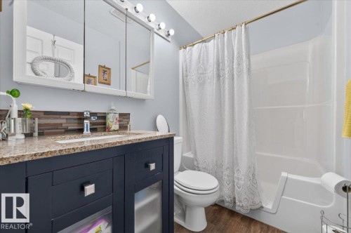 Bathroom featuring a navy vanity, speckled countertop, rectangular undermount sink, and a three-door mirrored medicine cabinet with integrated lighting - #125 4610 50 Ave, Stony Plain, AB 