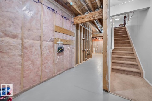Unfinished basement with exposed ceiling joists and wood framing, insulated walls, and a finished staircase with carpeted treads - #125 4610 50 Ave, Stony Plain, AB 