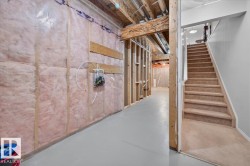Unfinished basement with exposed ceiling joists and wood framing, insulated walls, and a finished staircase with carpeted treads - 