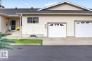 Two single-car garage doors with decorative lites, vinyl siding exterior, concrete steps with metal railing, and a gabled roofline - #125 4610 50 Ave, Stony Plain, AB 