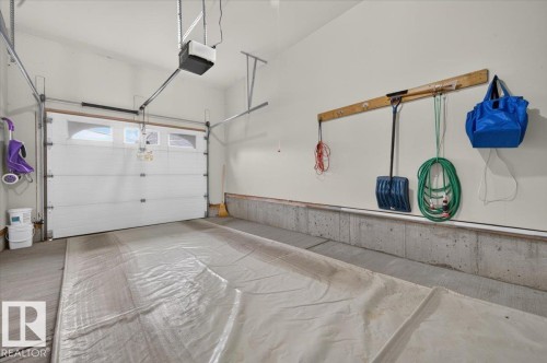 Attached garage with concrete flooring, overhead door with frosted glass panels, automatic garage door opener, and integrated wall-mounted storage rack - #125 4610 50 Ave, Stony Plain, AB 