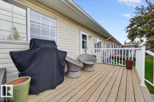 Wood-plank deck with white railing, featuring exterior siding and a clear glass paneled door - #125 4610 50 Ave, Stony Plain, AB 