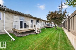 Expansive green space featuring a wood deck with white railings, mature tree, and a wood privacy fence on a concrete retaining wall - 