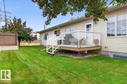 Rear exterior featuring a raised wooden deck with white railings, a ground-level patio, and a well-maintained lawn - 
