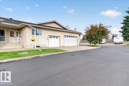 Two-car attached garage, paved driveway, mature trees, manicured lawn, and exterior siding - #125 4610 50 Ave, Stony Plain, AB 