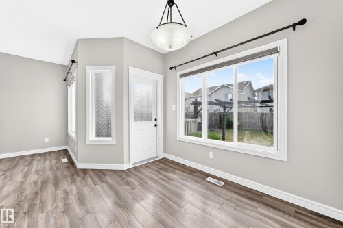 Wood-finish flooring, white trim, a single-panel door with decorative glass, and a large multi-pane window - Edmonton, AB 