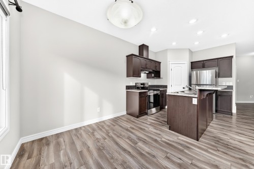 Kitchen featuring dark wood cabinetry, stainless steel appliances, an island with a sink, wood-finish flooring, and recessed lighting - Edmonton, AB 