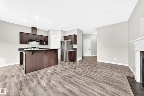 Open-concept living area featuring wood-finish flooring, recessed lighting, a kitchen island with dark wood cabinetry, and stainless steel appliances - Edmonton, AB 