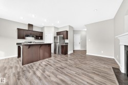 Open-concept living area featuring wood-finish flooring, recessed lighting, a kitchen island with dark wood cabinetry, and stainless steel appliances - 