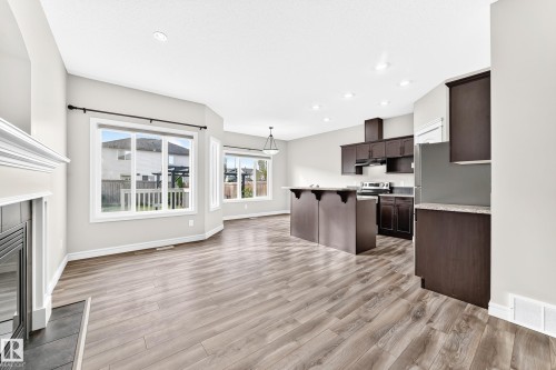 Open-concept living space featuring wood-finish flooring, a fireplace with a white mantel, and multiple windows - Edmonton, AB 