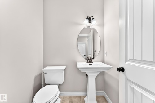 White pedestal sink with a dark bronze faucet, oval wall mirror, and a two-bulb vanity light - Edmonton, AB 