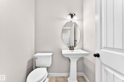 White pedestal sink with a dark bronze faucet, oval wall mirror, and a two-bulb vanity light - 