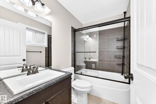 Bathroom featuring a dark wood-finish vanity, integrated sink, and an enclosed tub and shower combination with tile surround - Edmonton, AB 