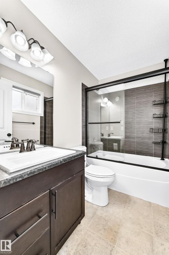 Bathroom featuring a dark wood-finish vanity, integrated sink, and a combination tub and shower with glass enclosure - Edmonton, AB 