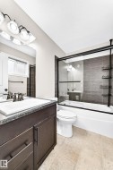 Bathroom featuring a dark wood-finish vanity, integrated sink, and a combination tub and shower with glass enclosure - 