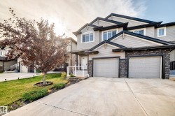 Grey siding exterior with dark stone accents, two attached garages, a concrete driveway, and a welcoming front porch with white railings - 