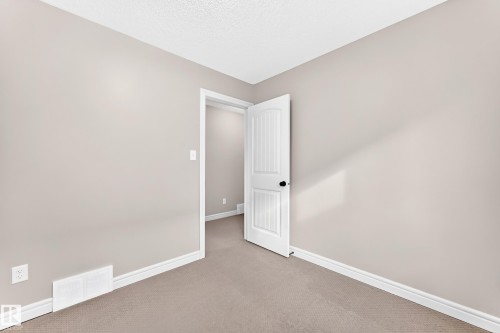 Soft neutral wall paint and carpeting, white trim, and a white paneled interior door with a black knob - Edmonton, AB 