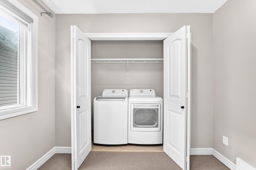 White bi-fold doors open to a laundry area with a white washer and dryer, complemented by a single wire shelf - Edmonton, AB 