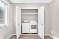 White bi-fold doors open to a laundry area with a white washer and dryer, complemented by a single wire shelf - 
