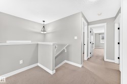 Carpeted landing featuring a contemporary pendant light fixture, white trim, and multiple doorways - 