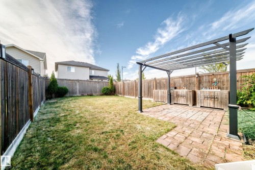 Expansive backyard featuring a pergola-covered patio with brick pavers, two built-in wood-paneled outdoor bar units, and a wooden perimeter fence - Edmonton, AB 