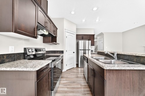 Kitchen featuring wood-finish flooring, dark wood cabinetry, light-toned countertops, and stainless steel appliances - Edmonton, AB 