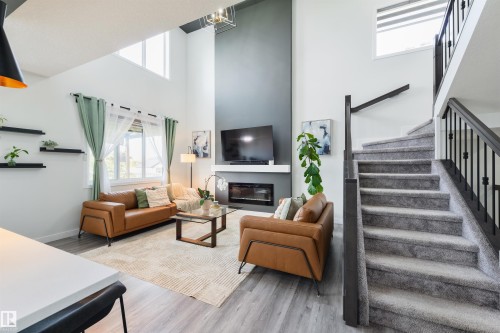 Living area with high ceilings, an electric fireplace, light wood-finish flooring, and a carpeted staircase with black metal balusters - 1032 Berg Place, Leduc, AB 