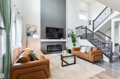 High ceilings with light walls, built-in fireplace, open staircase with dark wood-finish banister and metal spindles, and wood-finish flooring - 1032 Berg Place, Leduc, AB 