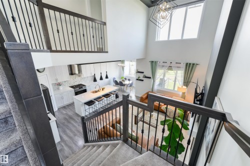 Open-concept living space featuring a two-story ceiling, a contemporary kitchen with a center island and stainless steel appliances, and a staircase with dark wood railings and black spindles - 1032 Berg Place, Leduc, AB 
