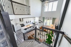 Open-concept living space featuring a two-story ceiling, a contemporary kitchen with a center island and stainless steel appliances, and a staircase with dark wood railings and black spindles - 