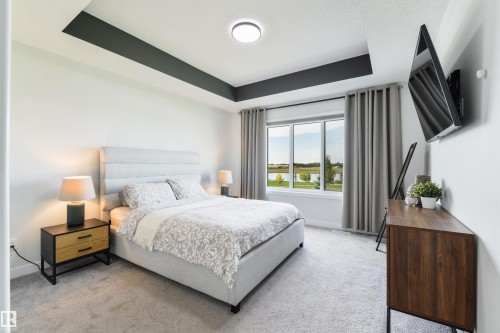 Tray ceiling with accent paint, large window with outdoor scenery, wall-mounted television, and light-colored carpet flooring - 1032 Berg Place, Leduc, AB 