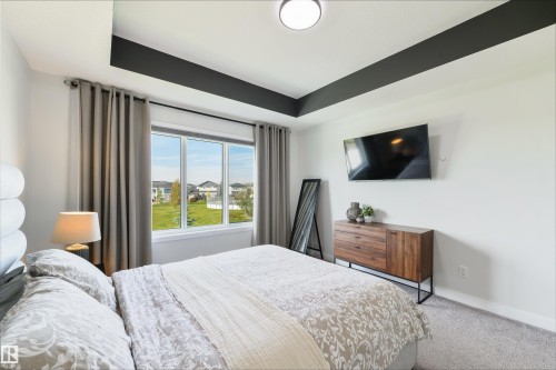 Tray ceiling with dark accent, wall-mounted television, large window, and carpeted flooring - 1032 Berg Place, Leduc, AB 