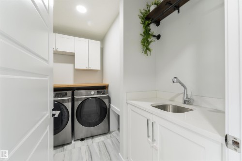 Wood-finish countertop, white upper cabinetry, built-in sink with a pull-down faucet, white lower cabinetry, and wood-finish flooring - 1032 Berg Place, Leduc, AB 