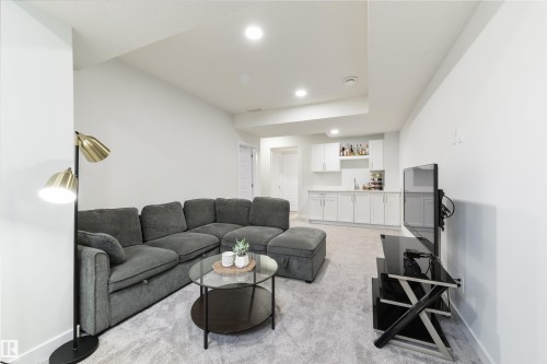 Recessed lighting illuminates the carpeted living area with a built-in wet bar featuring white cabinetry and a sink - 1032 Berg Place, Leduc, AB 
