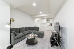 Recessed lighting illuminates the carpeted living area with a built-in wet bar featuring white cabinetry and a sink - 