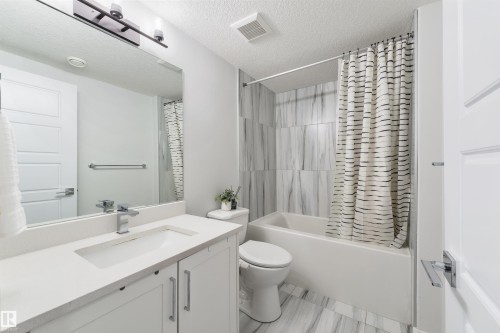 Bathroom featuring a white vanity with an integrated sink, polished chrome faucet, white paneled cabinetry, and a full-width mirror - 1032 Berg Place, Leduc, AB 