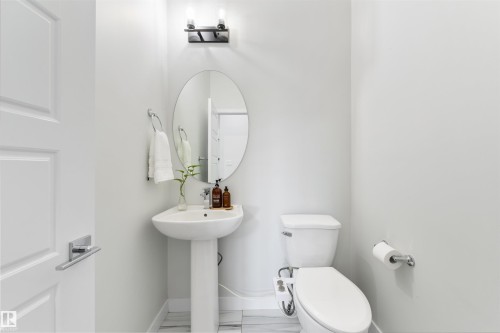 Pedestal sink with an oval mirror, modern wall-mounted light fixture, and tile flooring - 1032 Berg Place, Leduc, AB 