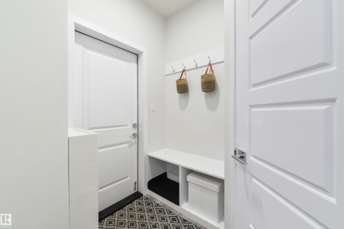 Entryway featuring a built-in bench, wall-mounted coat rack, white paneled doors, and patterned floor tile - 1032 Berg Place, Leduc, AB 