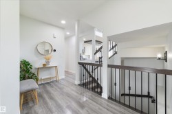 Wood-finish flooring, recessed lighting, white walls, and a staircase with dark wood handrails and black metal spindles - 
